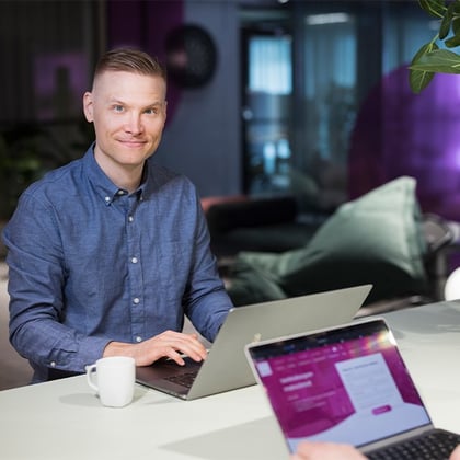 Man sitting at a table with a laptop and looking at the camera