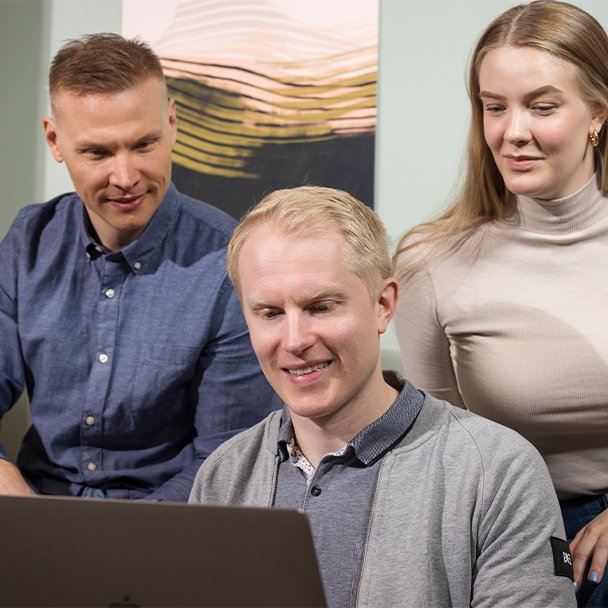 Three people sitting together and looking at the same laptop screen.