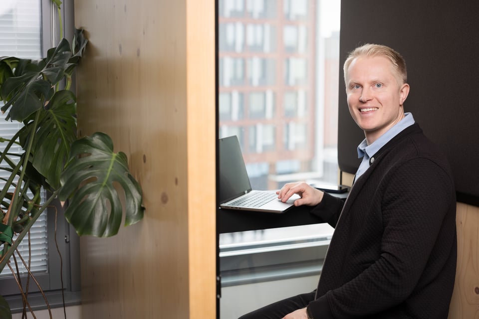 Smiling person sitting at a laptop by a window in an office setting