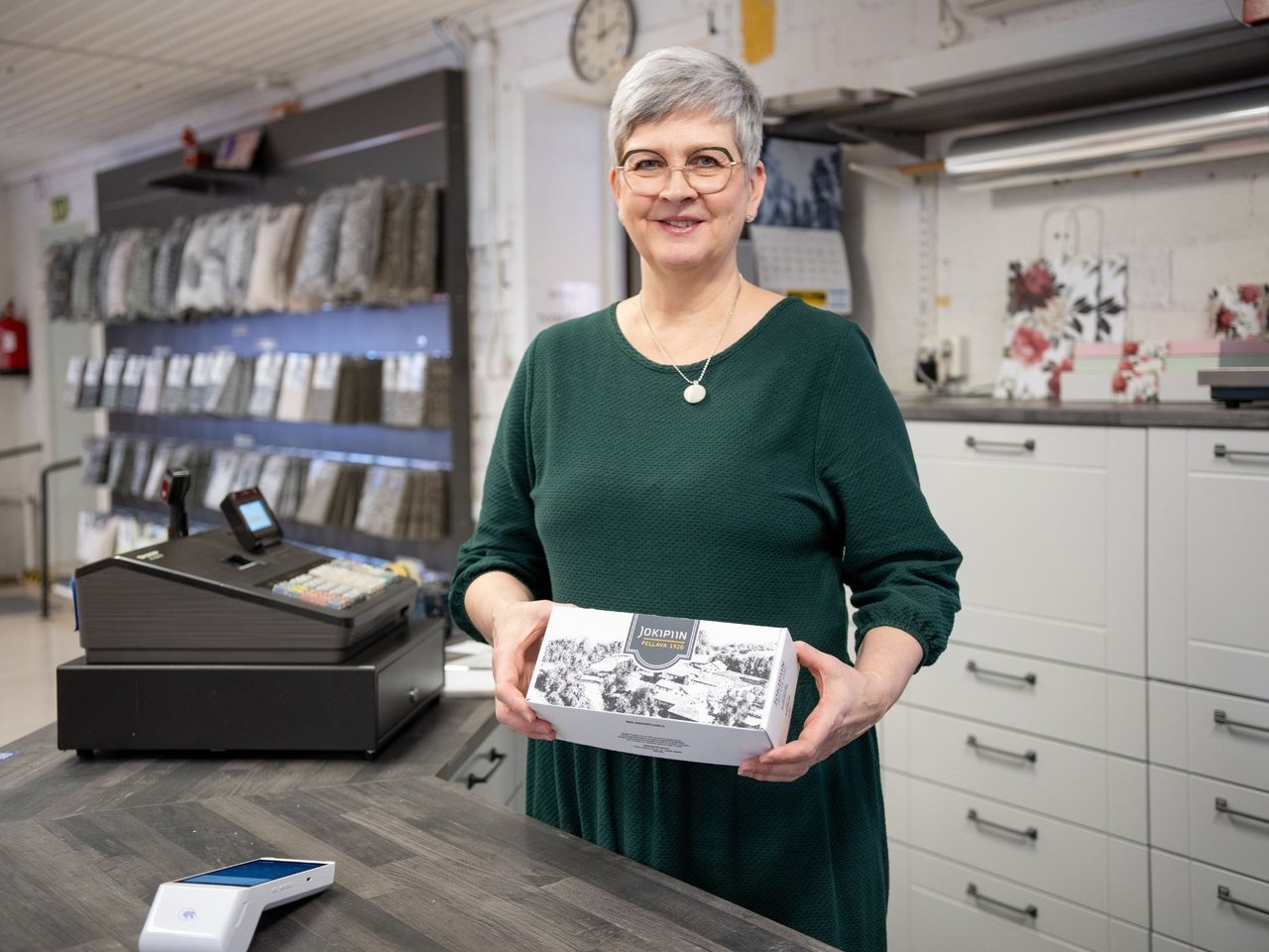 Työntekijä kassalla maksupäätteen ja tuotteen kanssa