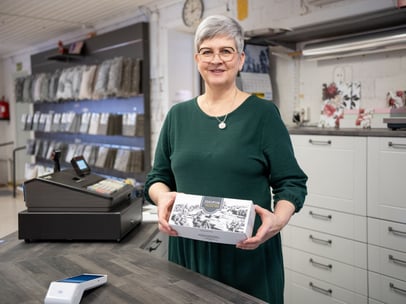 Työntekijä kassalla maksupäätteen ja tuotteen kanssa