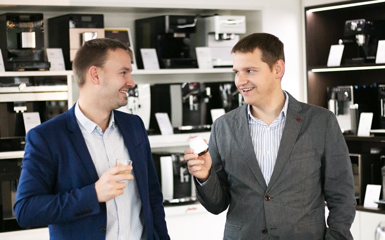 Two men smiling and holding coffee cups in a coffee machine Kahvikaveri's showroom